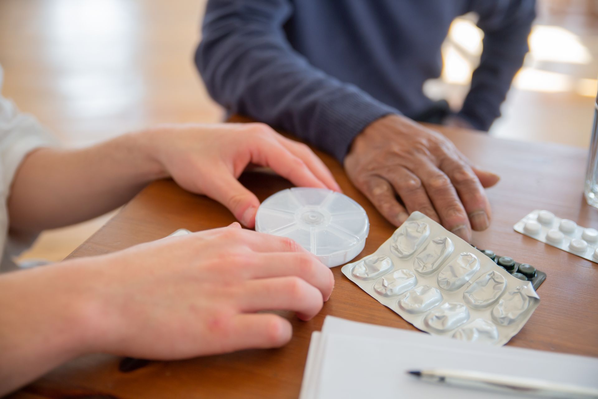 Mãos junto a um porta-comprimidos e cartelas de medicamentos sobre a mesa.