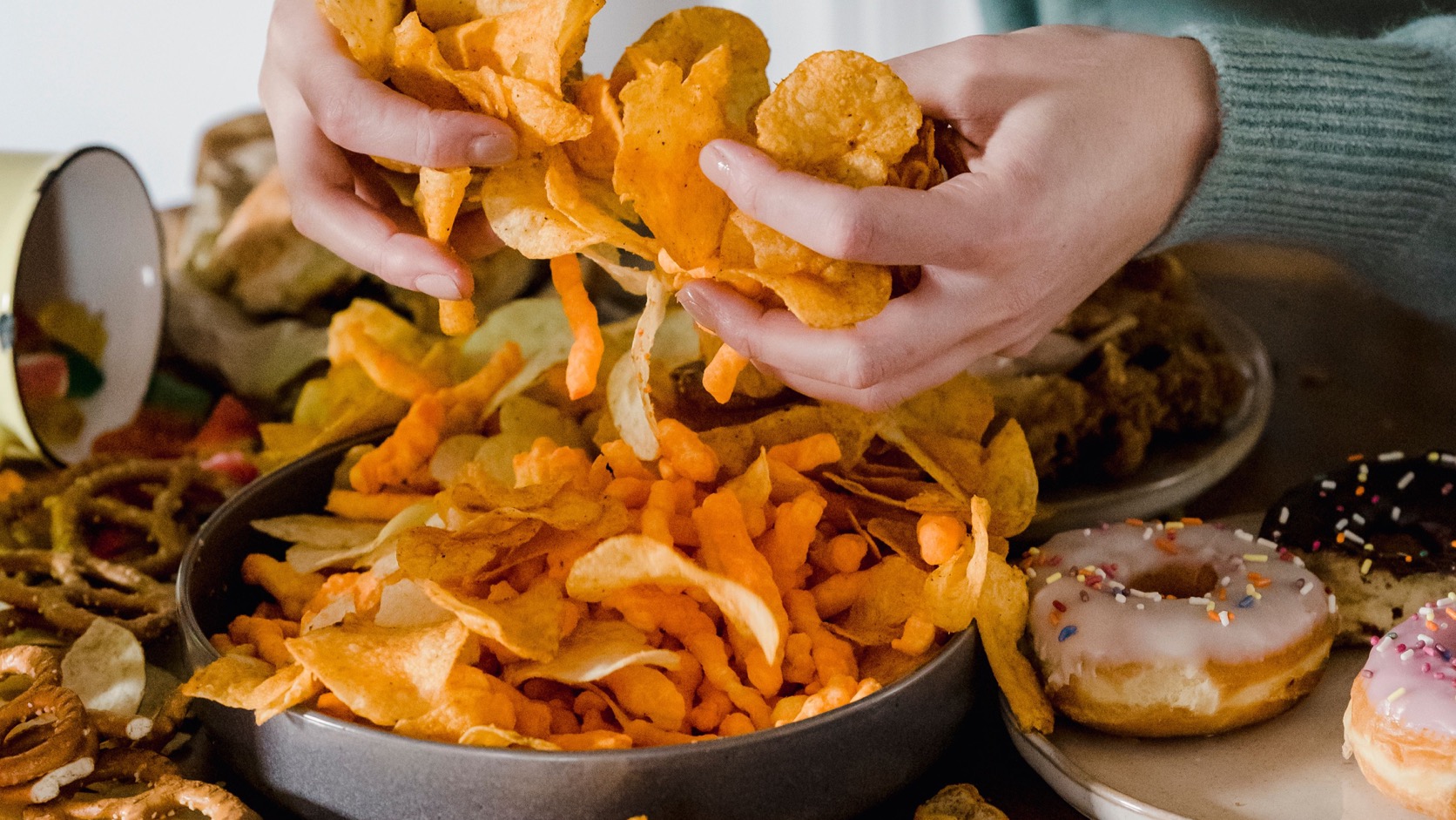 Pessoa segurando salgadinhos diante de diferentes alimentos sobre a mesa