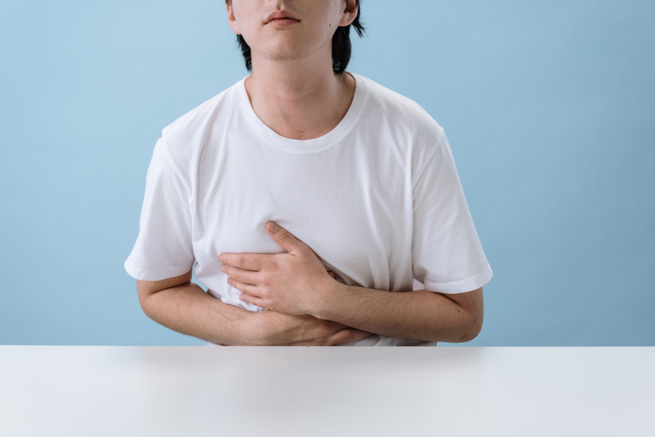Pessoa de camiseta branca com as mãos sobre a região do estômago.