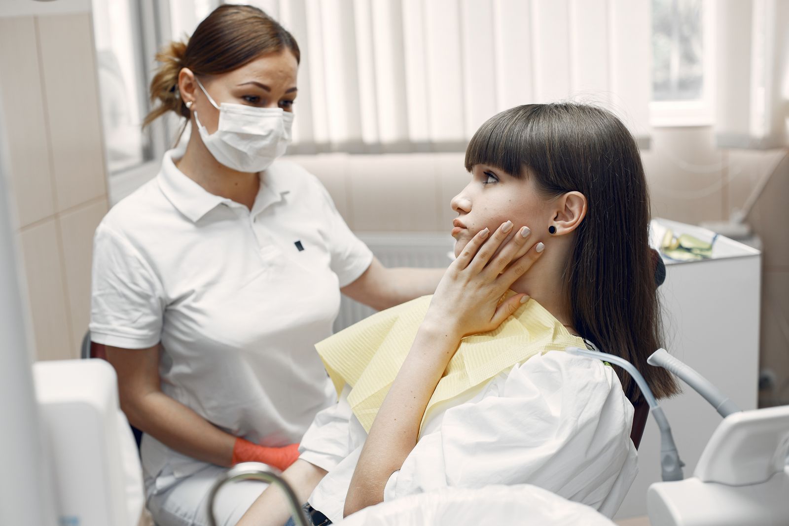Mulher toca a região da mandíbula enquanto é atendida por uma dentista.