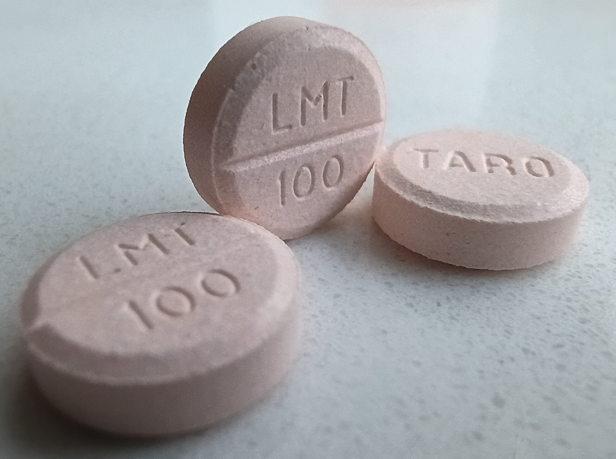 Três comprimidos rosados de lamotrigina sobre uma superfície clara.
