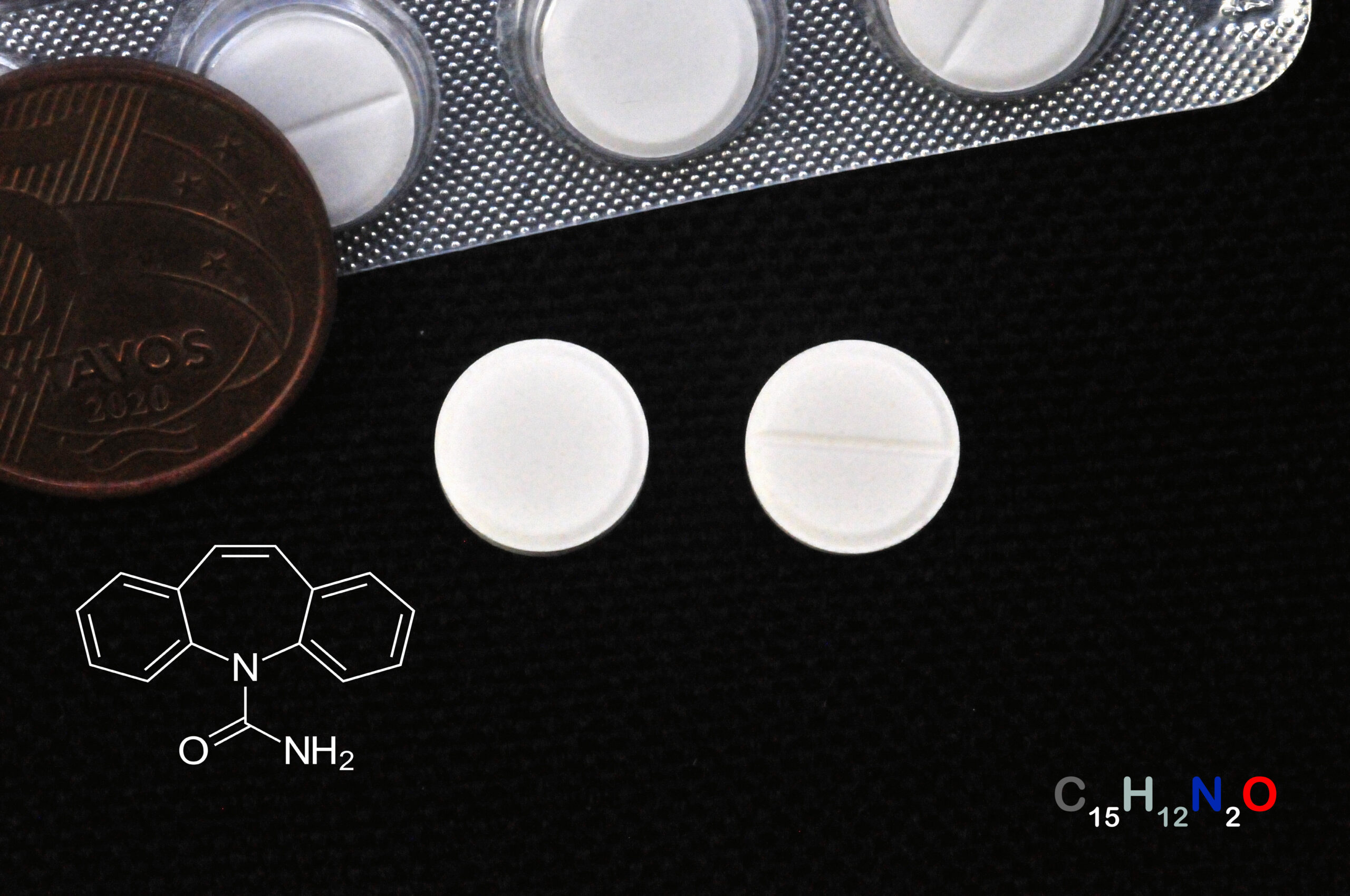 Cartela e comprimidos de carbamazepina, com moeda para comparação de tamanho e fórmula química.