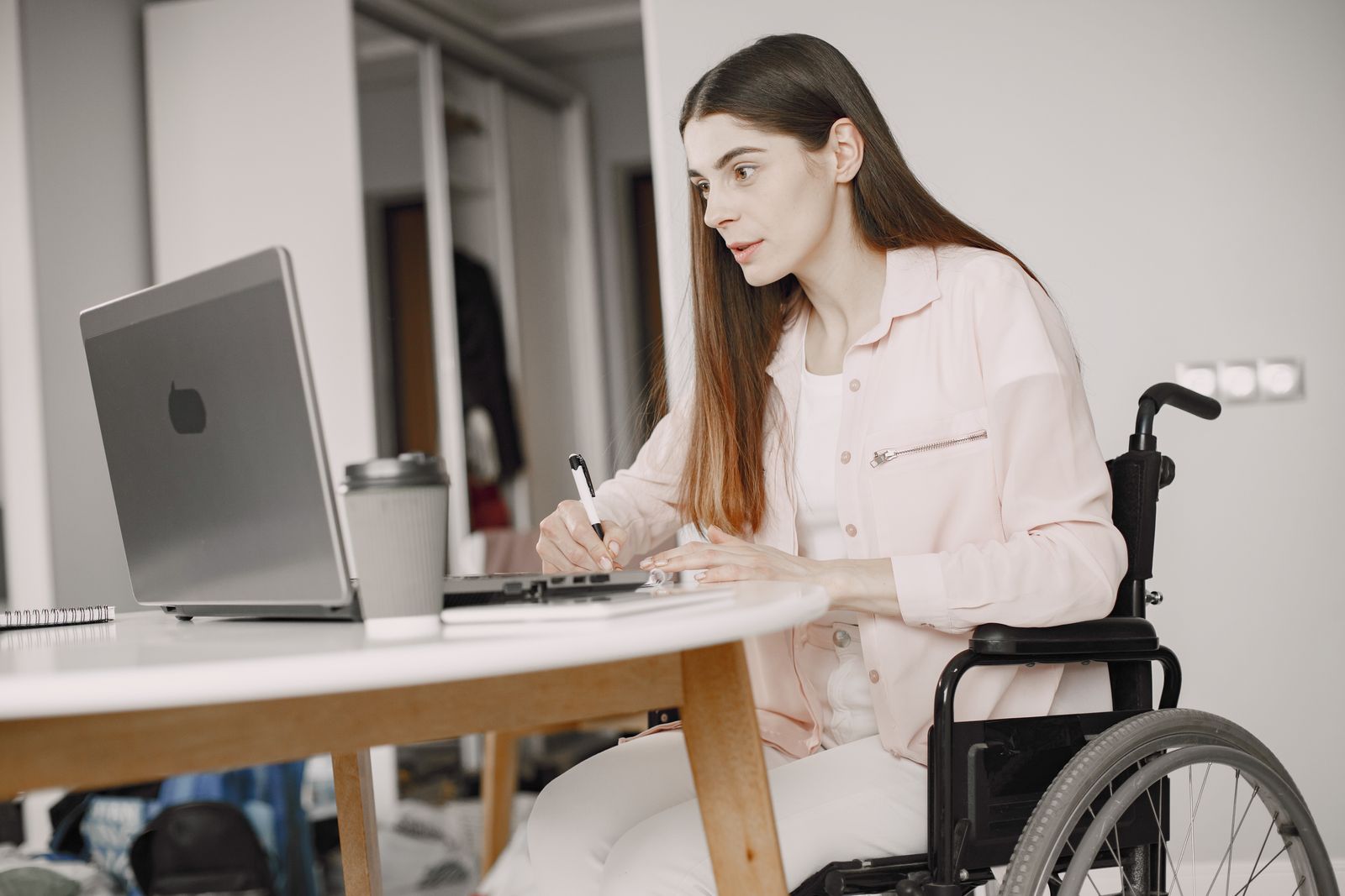 Mulher em cadeira de rodas faz anotações enquanto olha para um notebook.