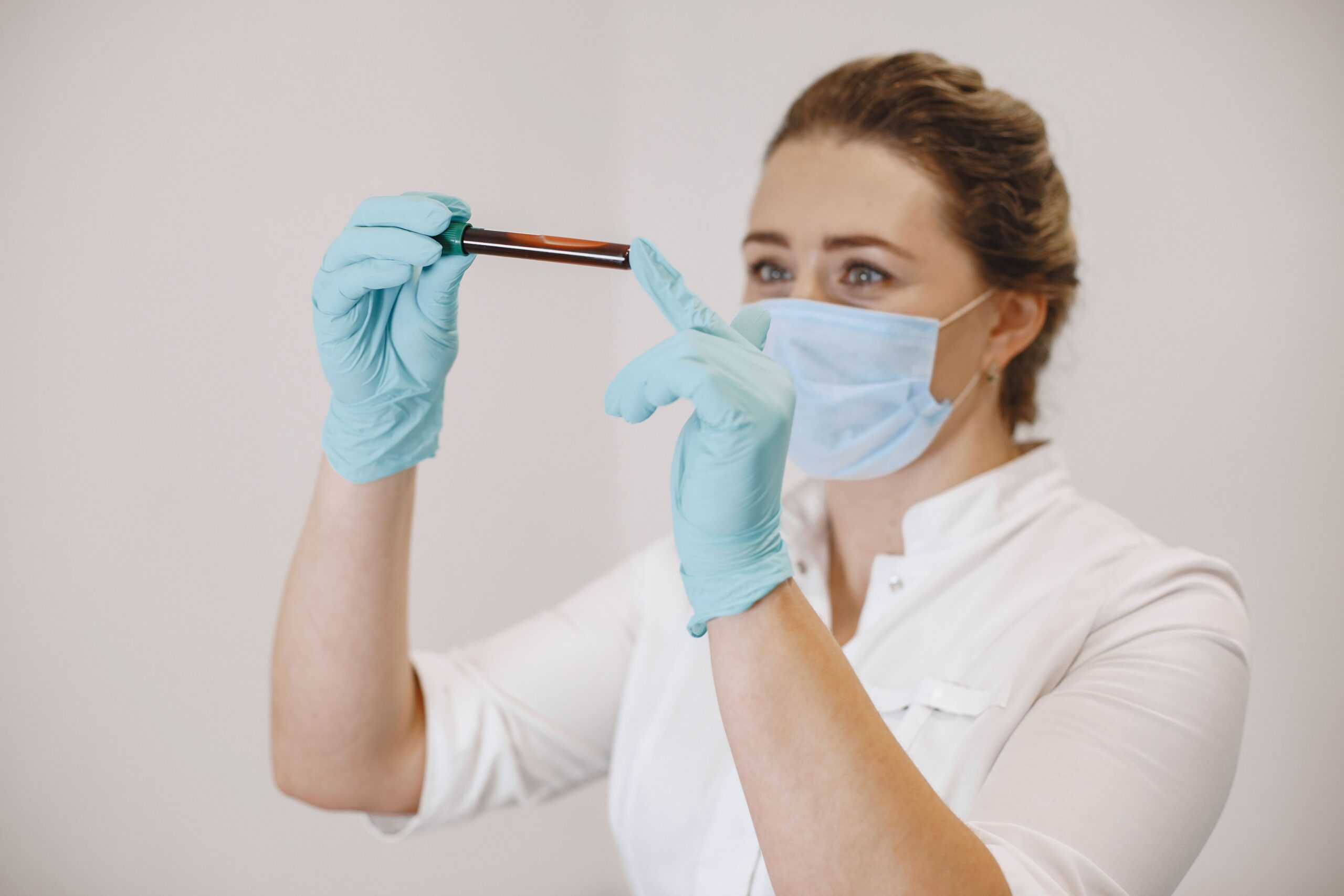 Profissional com máscara e luvas segura um tubo com amostra de sangue.
