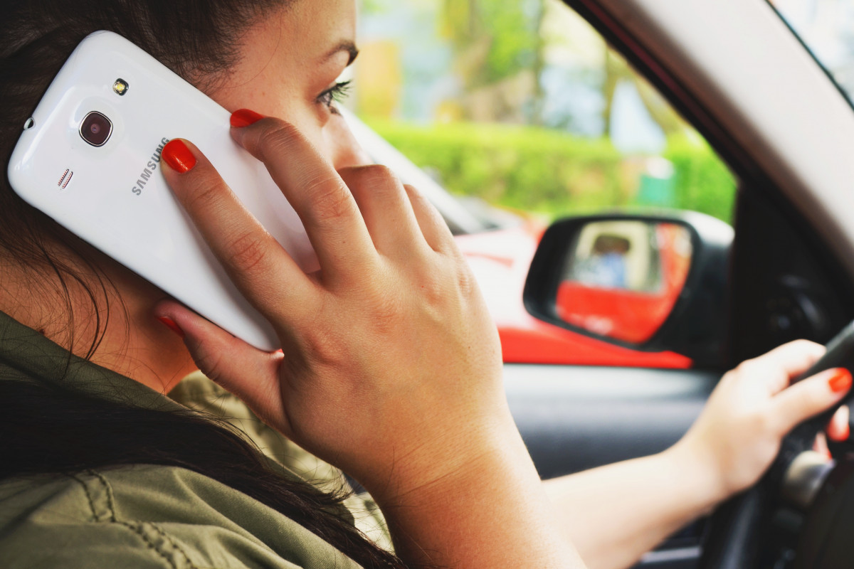 Mulher no banco do motorista segura um telefone próximo ao ouvido.