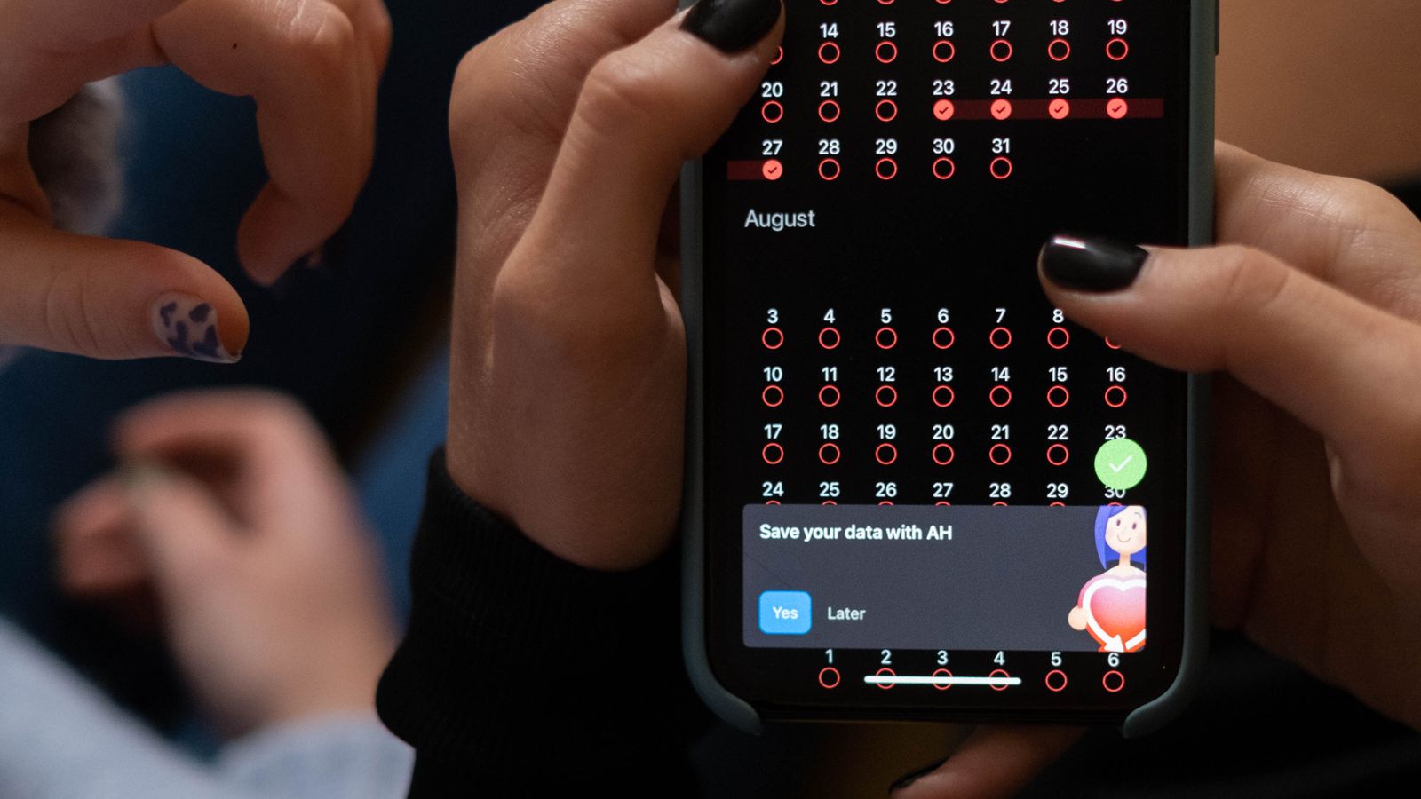 Mãos seguram um celular com calendário de acompanhamento do ciclo menstrual.