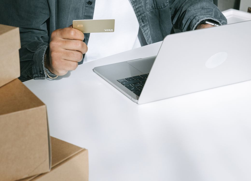 Pessoa usa cartão próximo ao computador e a caixas de encomendas.