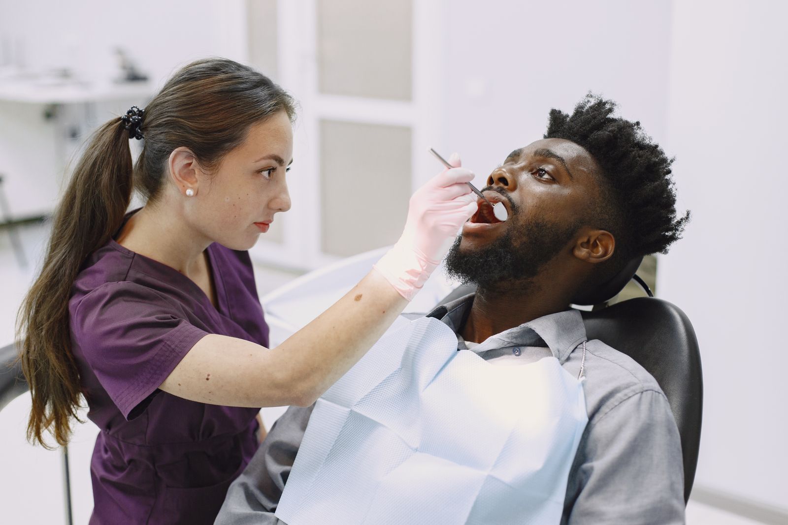 Dentista examina a boca aberta de um homem sentado na cadeira odontológica.