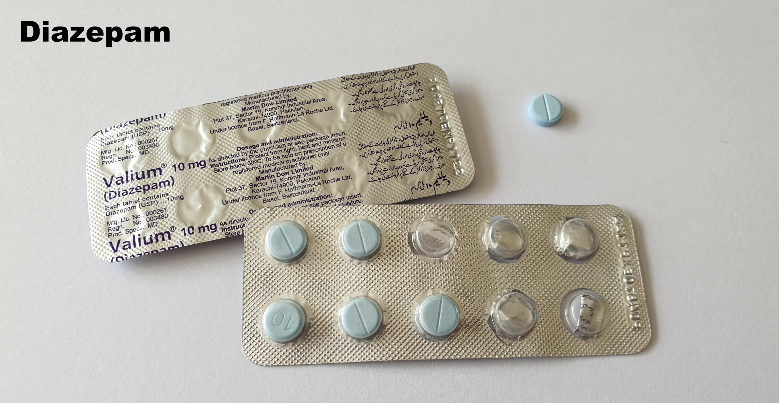 Cartelas de diazepam com comprimidos azuis sobre uma superfície escura.