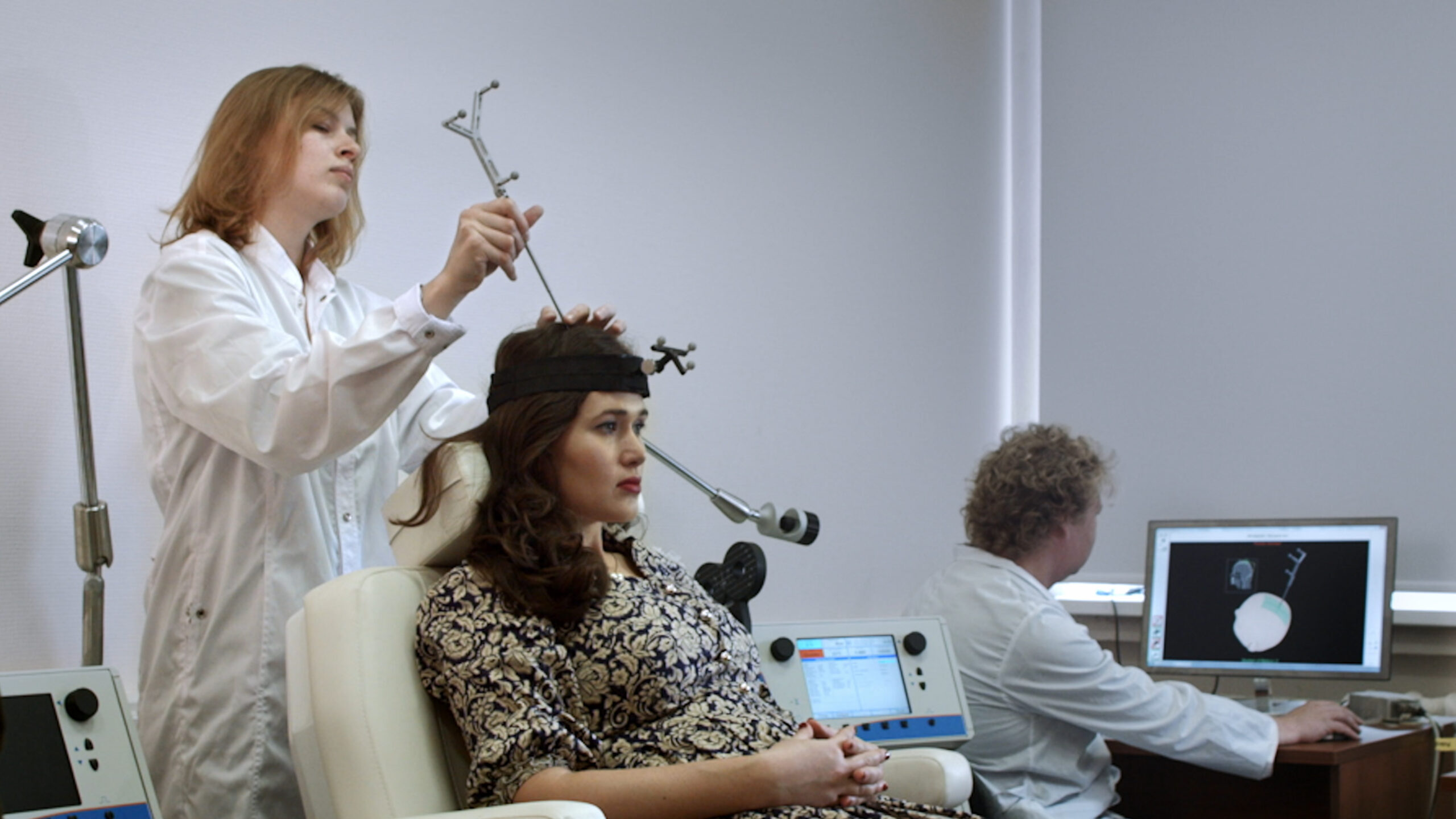 Preparação para estimulação magnética transcraniana em laboratório, com equipamentos de posicionamento e monitor.
