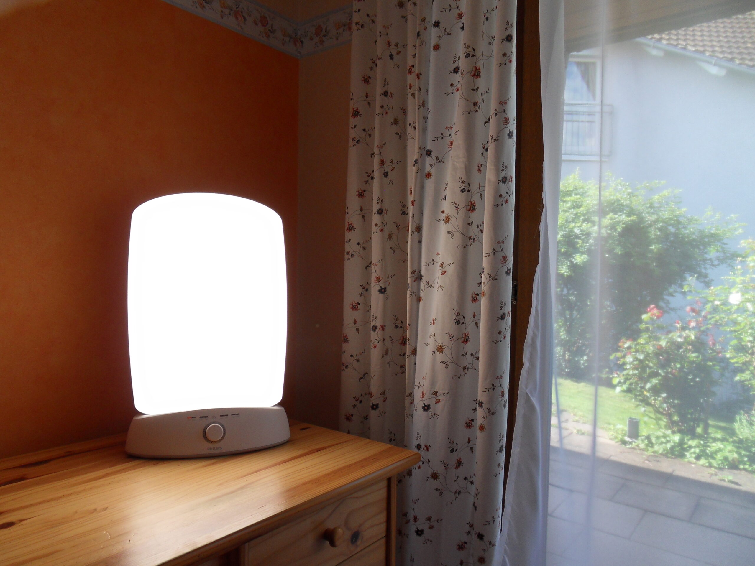Painel de fototerapia com luz branca sobre uma mesa, próximo a uma janela.