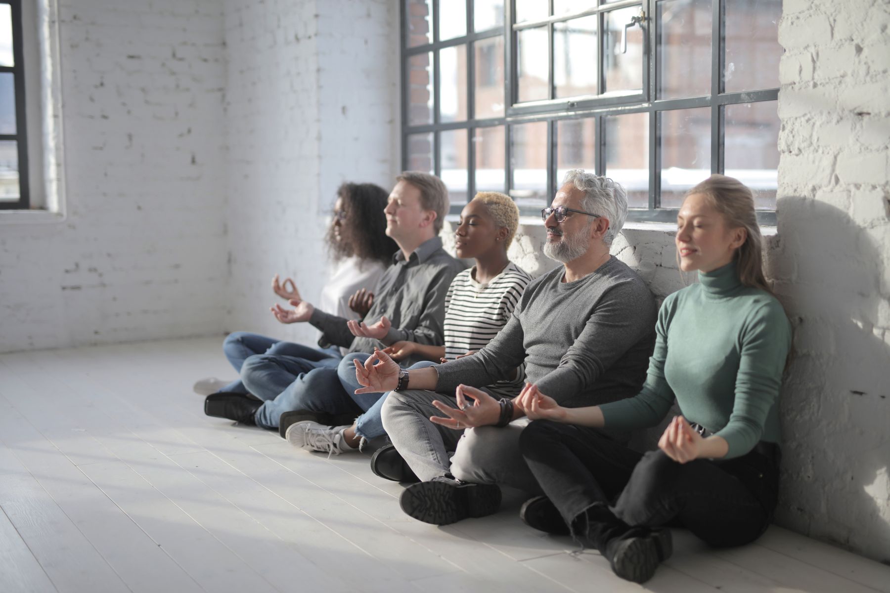 Grupo de adultos sentados no chão, de olhos fechados, durante uma prática de meditação.