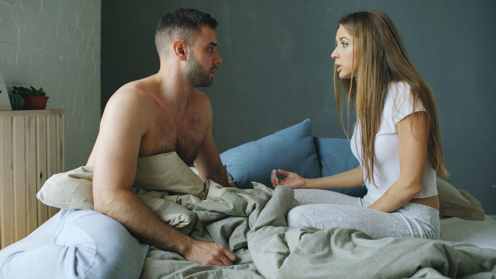 Casal sentado na cama, conversando frente a frente.