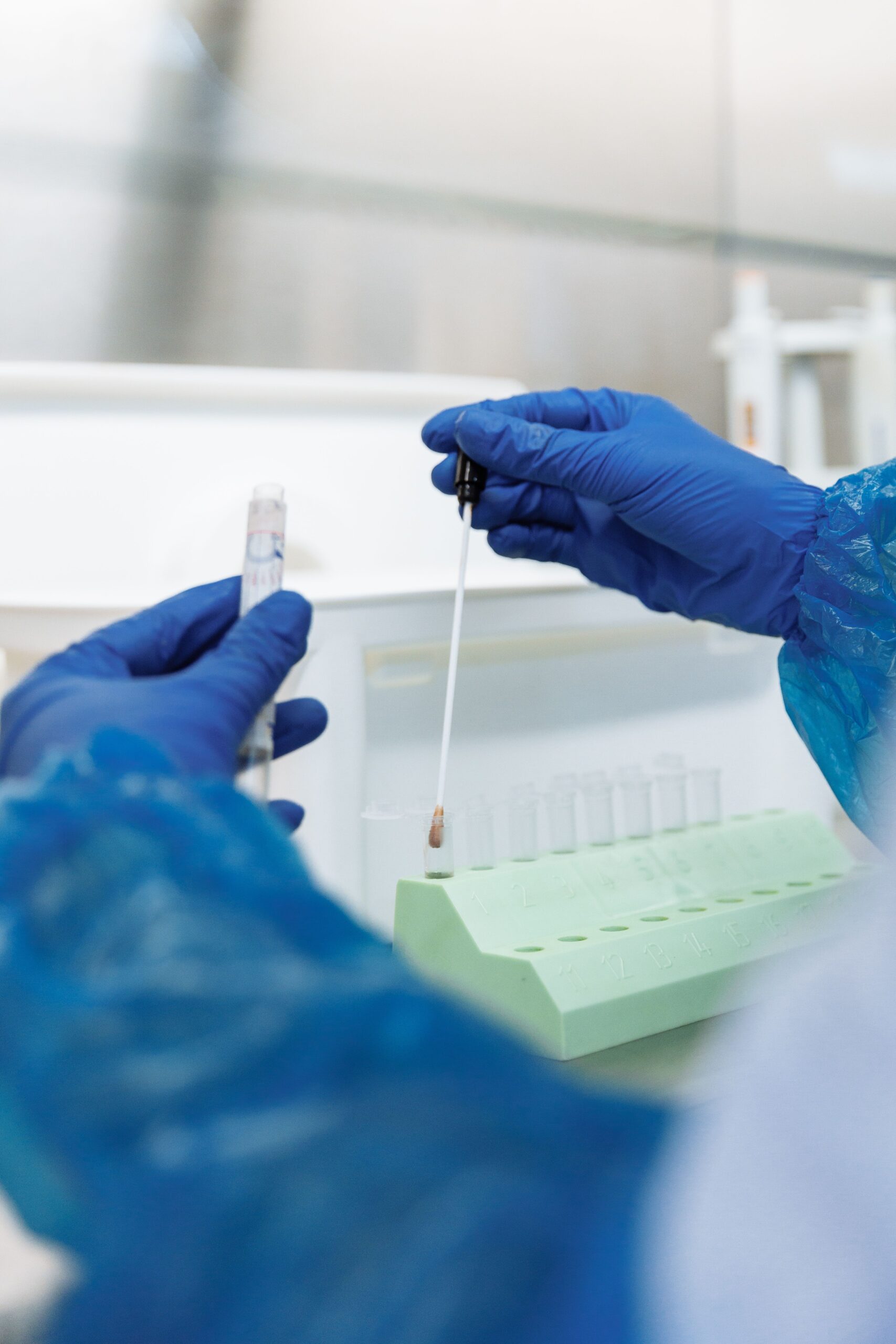 Mãos com luvas manuseando um swab e tubos de amostras em laboratório.