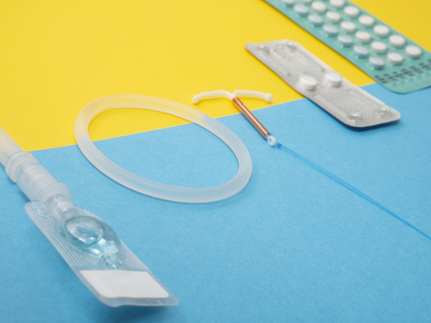 Anel vaginal, DIU, cartelas e outros contraceptivos sobre fundo azul e amarelo.